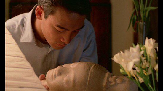 still of Mui's employer holding a bust of the Buddha and looking at the expression